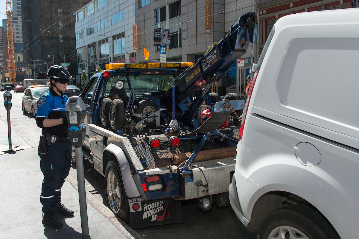 Photo of parking control officer issuing a citation while a tow truck prepares to tow away a van