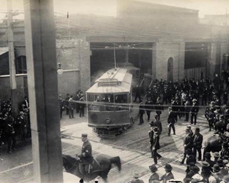 Archival photo from 1907 depicting a streetcar in San Francisco on Turk and Fillmore Streets under police protection during the deadly URR strike