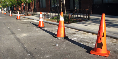 A row of parking cones block parking at the curb. The last cone has a jack-o-lantern face.