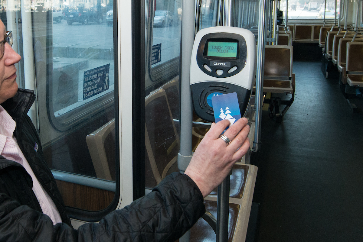 Person sitting on a bus taps their clipper card.