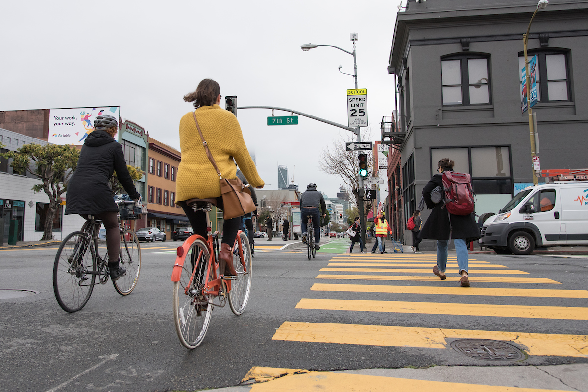 People walking and on bicycles in the street and crosswalk. 