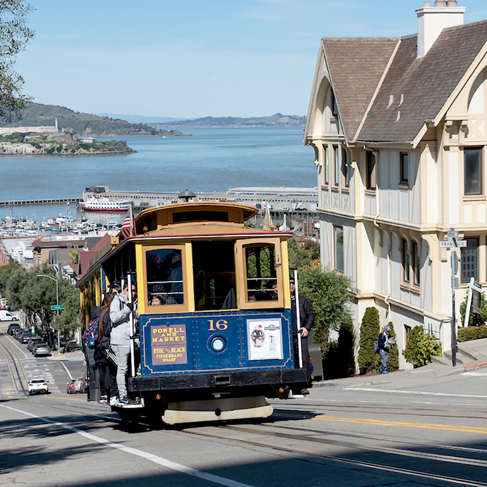 Color photo of cable car 16 climbing hill on Hyde Street with view of San Francisco Bay in background.