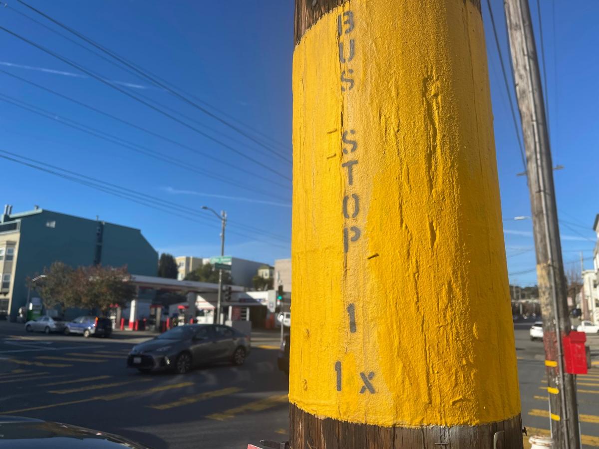 Photo showing a pole on the street painted yellow that says bus stop, 1, 1X