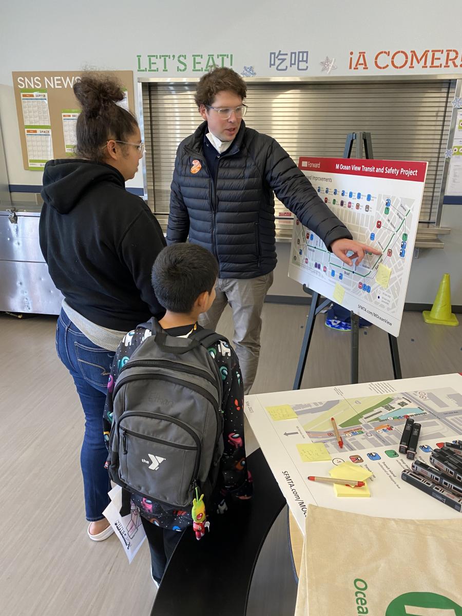 Project staff points at a poster about the project and speaks with a family at Sheridan Elementary School.