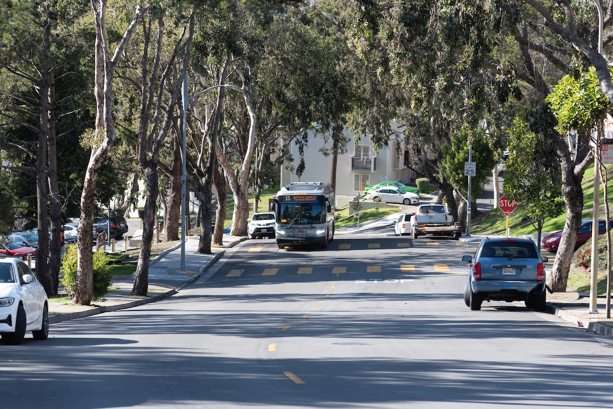 A 15 Bayview Hunters Point Express bus rides down a tree-lined street in San Francisco.