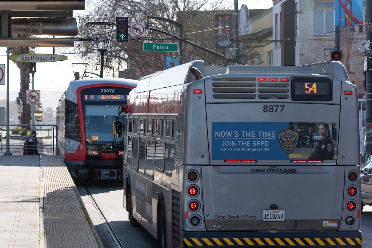 A bus and light rail vehicle at a stoplight near a transit platform during the day