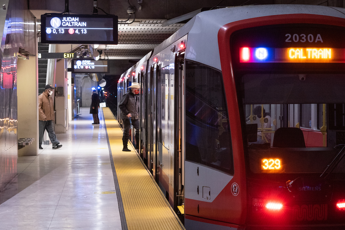 Several passengers are seen boarding a train in a subway. An overheard sign is above with lights.