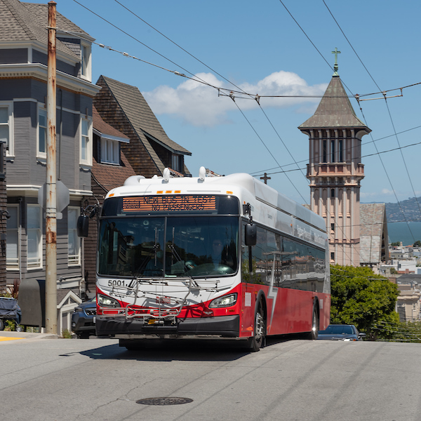 A red and white battery-electric bus climbs a steep street in San Francisco.