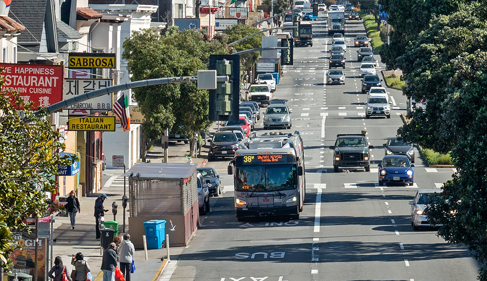 Overhead photo of Geary Boulevard showing Geary businesses, people visiting businesses and waiting for the bus, and 38R Geary Rapid bus driving in transit lane