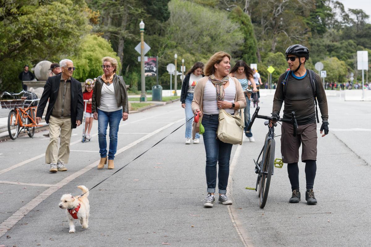 A group of people with a dog and a bicycle walking on JFK Promenade in Golden Gate Park