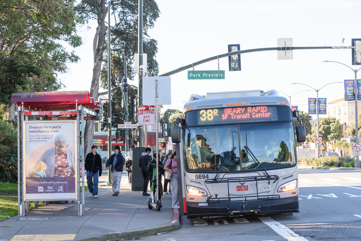 People board a 38R bus at Park Presidio and Geary. We see a bus shelter with an ad on it and Park Presidio on a green sign above the bus.