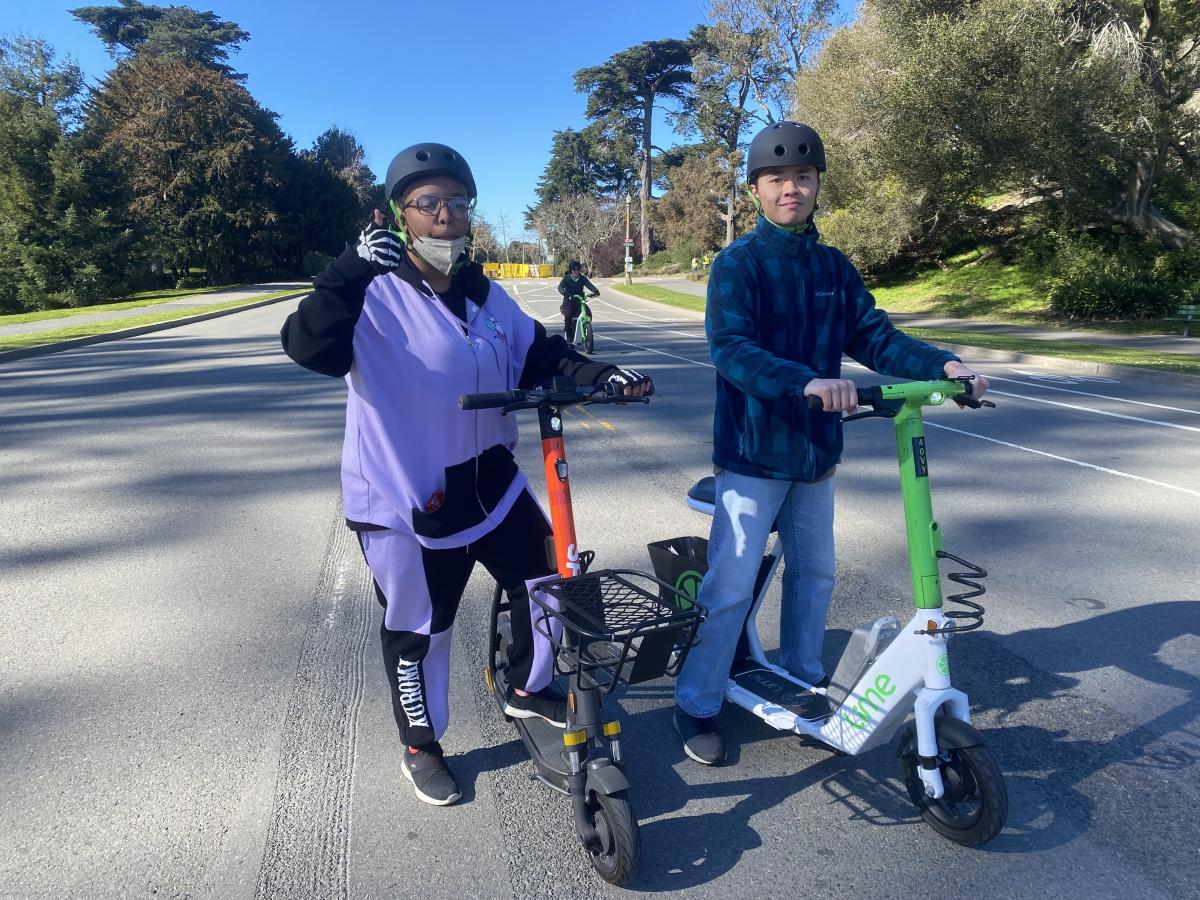AccessSFUSD students standing with Lime and Spin scooters; one student is giving a thumbs up