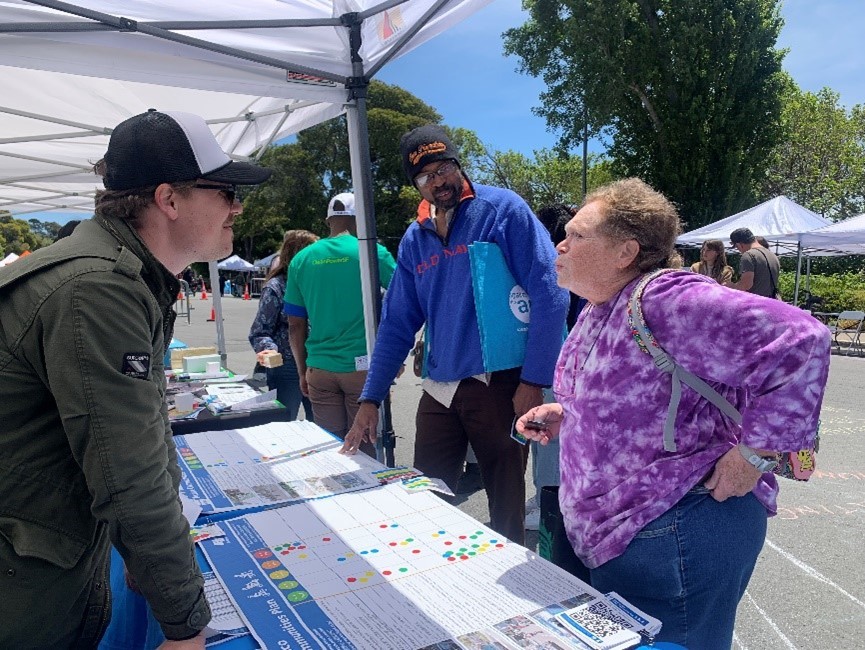 People talking under a tent with charts on a table and more tents in the background.