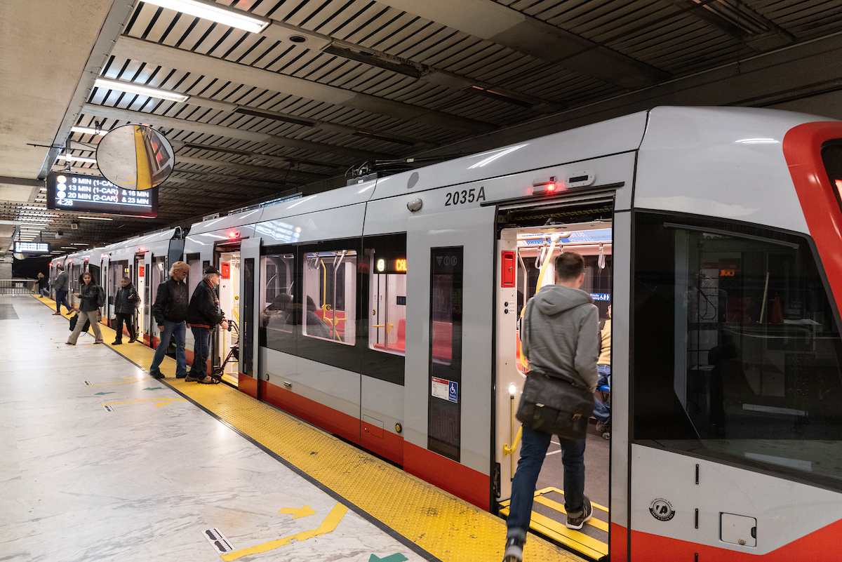 Image shows a train paused at a station platform; some customers enter and others exit