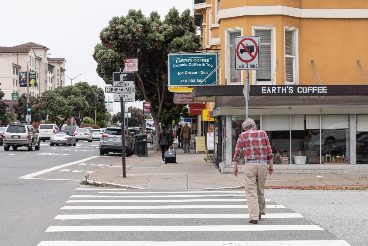 Image shows pedestrian crossing a continental crosswalk walk looking for oncoming traffic.