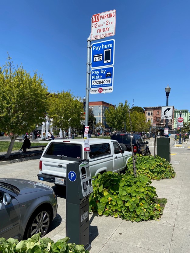 Cars parked along the sidewalk outside with pay station nearby and blue sky above.