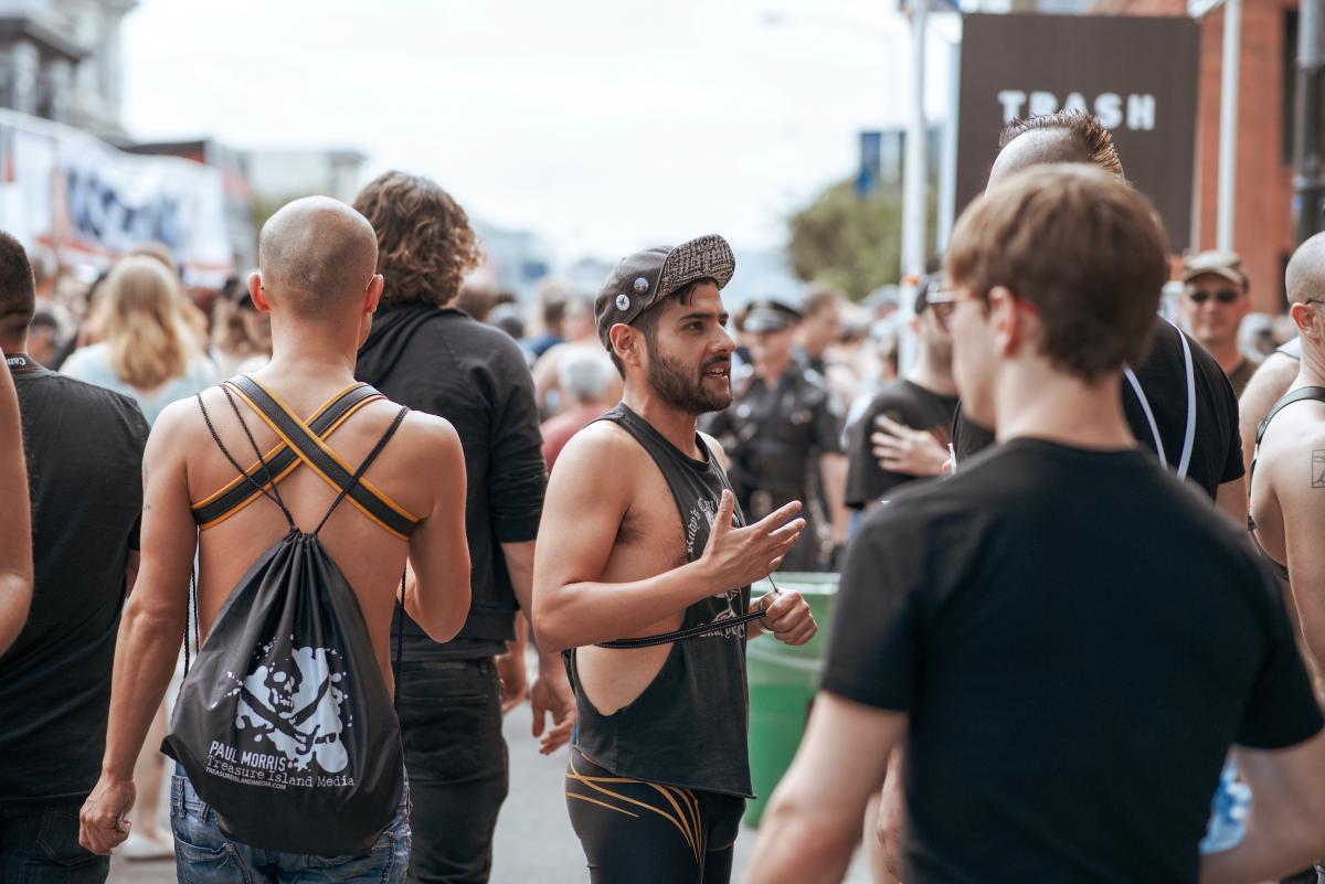 People attend the Folsom Street Fair. In the foreground we see people talking, walking and observing the crowd.