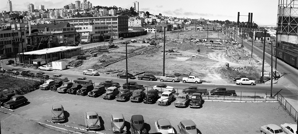 Black and white shot of Kirkland Yard. Dirt covers much of the site and classic cars are parked beside it. 