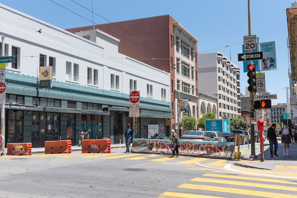 Image shows a person using a crosswalk in front of barricades that block off the street for the Golden Gate Greenway