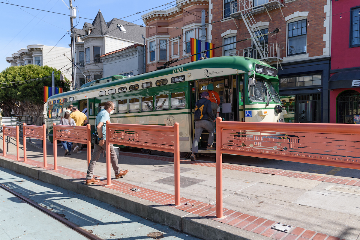 People, a platform, a streetcar and buildings in the daytime. 