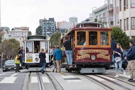 Two San Francisco Cable Cars on the tracks on the street with people boarding on and off.