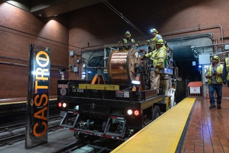 Workers on a truck in a subway station with a large roll of wiring