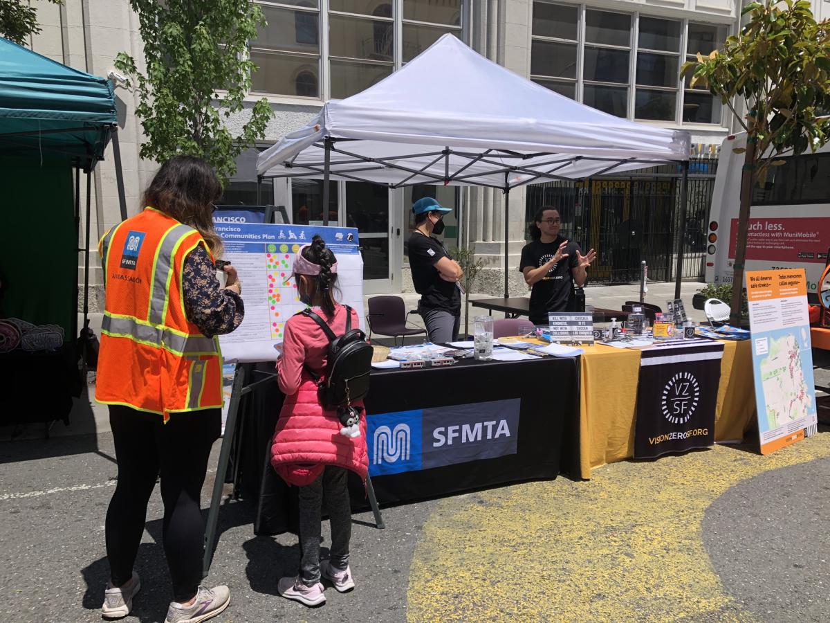 A woman in an orange SFMTA vest does a survey activity with a child at an outdoor table