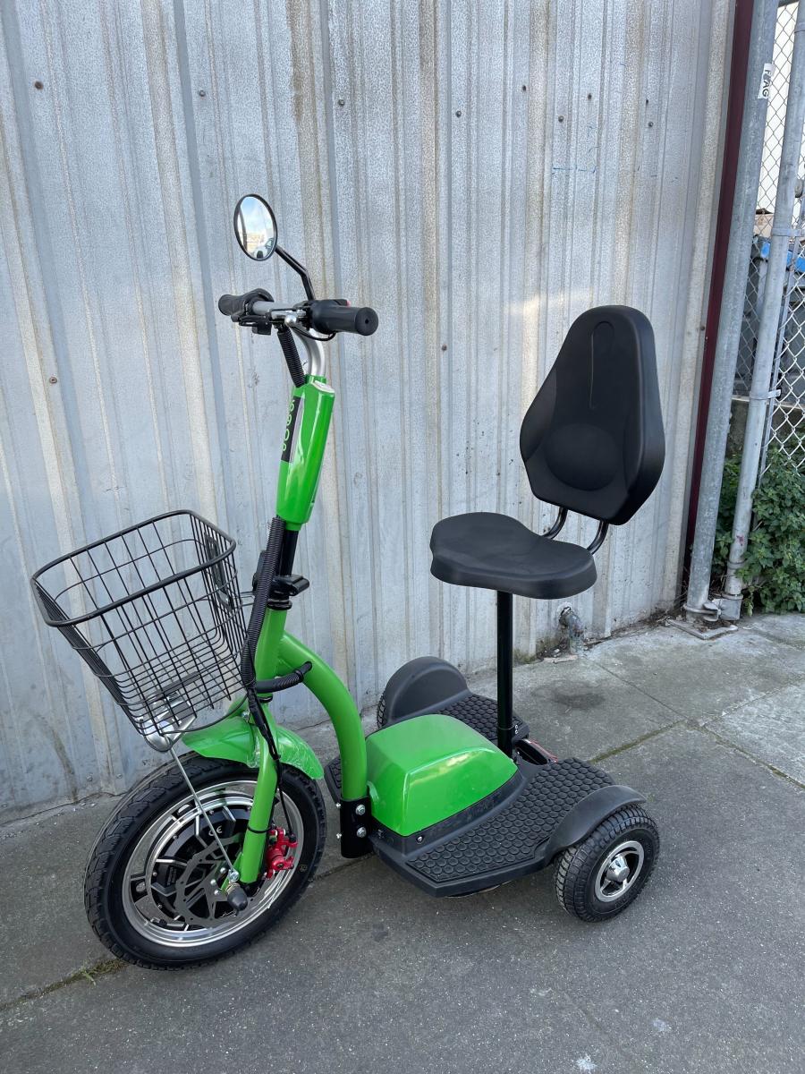 Lime green and black trike with wide footboard, seat with backing, and basket attached to the front of the device