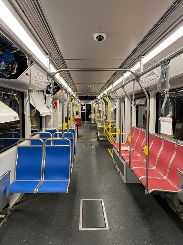 The interior of a train with blue double seats facing forward on one side and a row of red seats facing the aisle on the other.