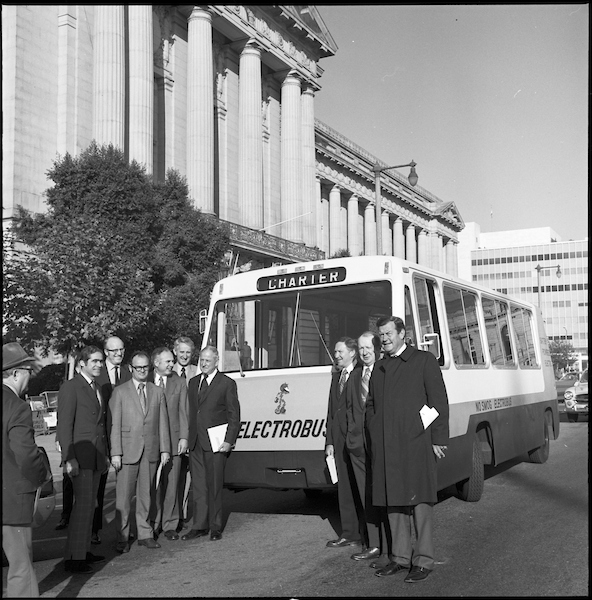 A black and white photo of an early-stage Electrobus with people posing for a photo around it.