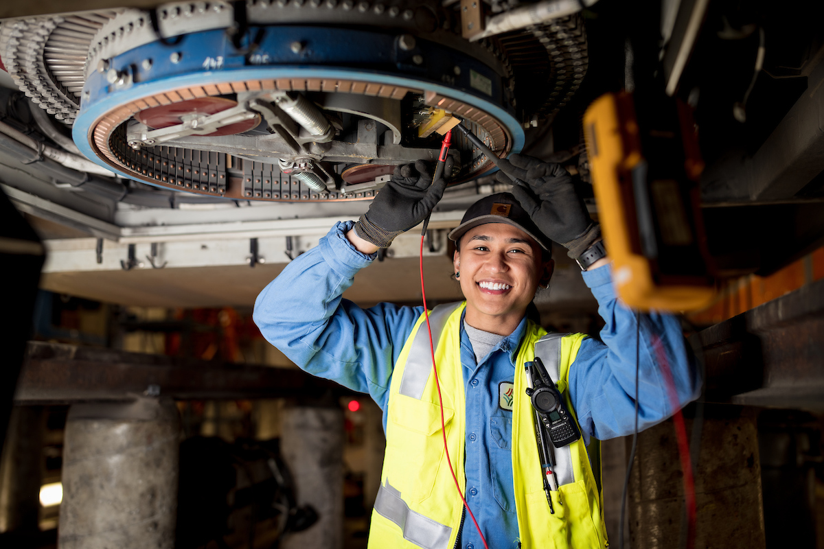 Jeena Villamor makes a repair for the SFMTA. She wears a yellow safety vest and works on overhead equipment. 