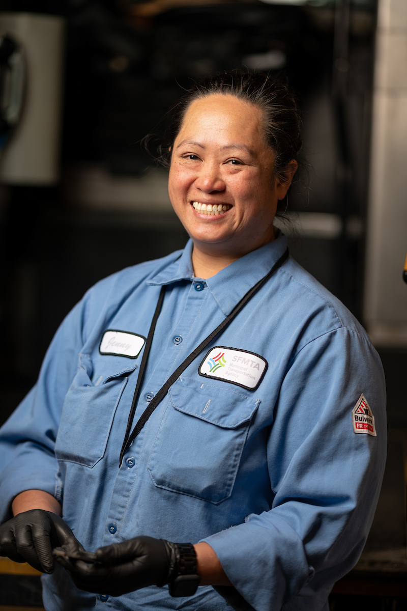 Jenny Keosaat smiles at the camera. She wears a blue uniform and black rubber gloves to make a repair.