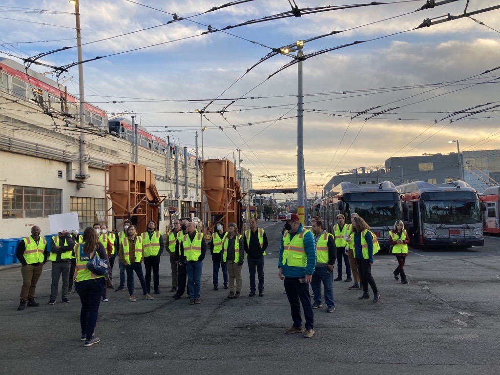 A group of people in yellow safety vests are seen in a transit facility