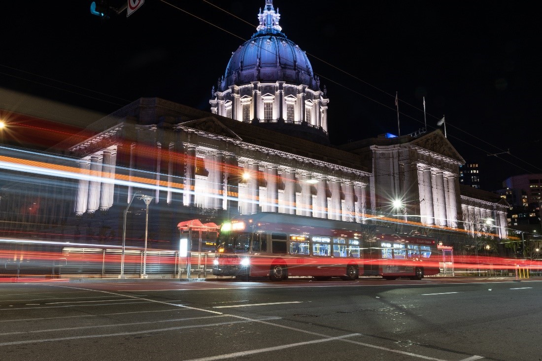A night time photo of San Francisco's city hall with a Muni bus driving by.