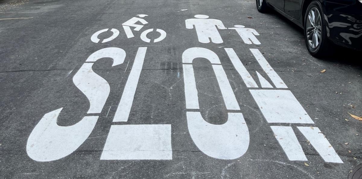 new slow streets program pavement markings show, in white, the outline of a person on a bike, an adult and a child, and the word SLOW
