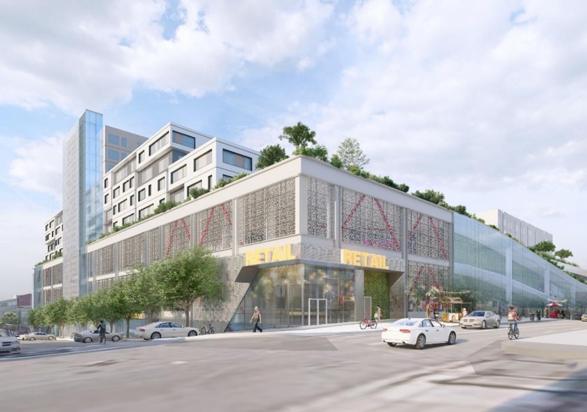 A rendered image of a modern multi-use building is seen from the street level intersection of 17th and Hampshire streets. At the corner, a retail establishment is seen. The first two levels of the building show industrial construction elements. Above those levels, housing units are seen along with greenery and trees. Pedestrians are seen on the sidewalk, a cyclist is seen in a bike lane, and vehicles are on the street.