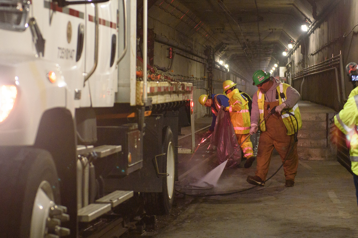 Several crew on spraying water on the tracks alongside a truck. 