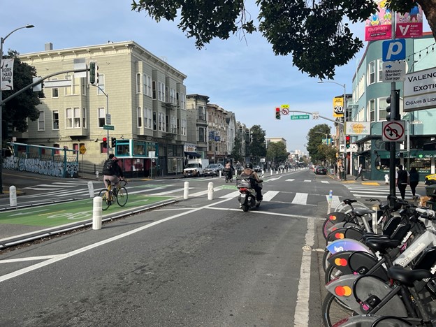 People bike down a center-running protected bike lane in the middle of a street with motorcycles and cars in the outer traffic lanes.