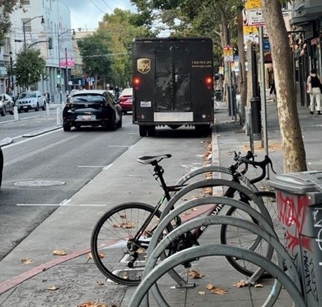 Parked bicycles on a sidewalk near cars and a delivery truck in a street. 