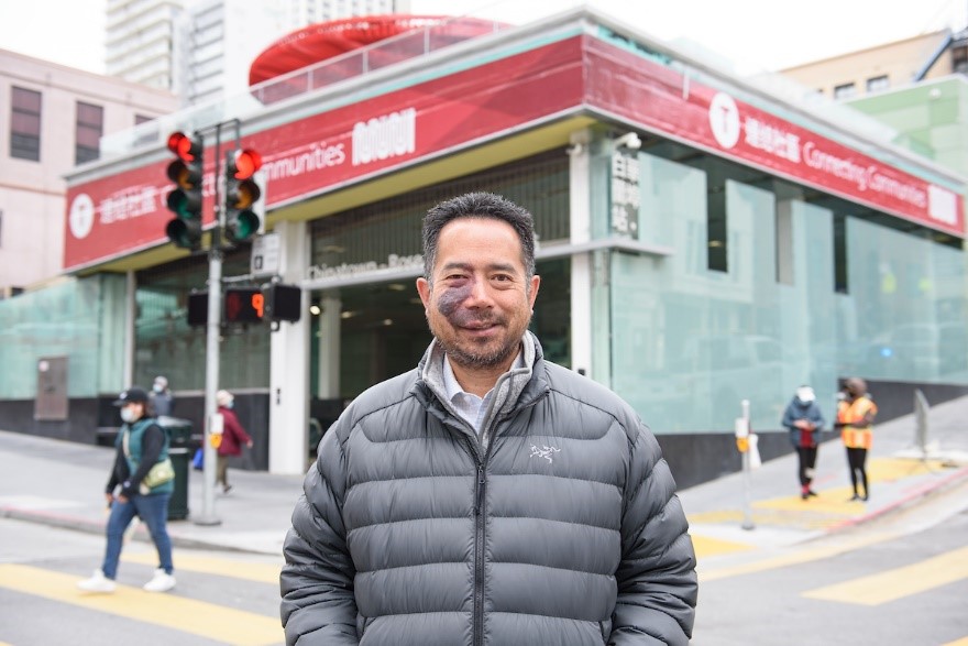 A man in a grey jacket standing in front of a transit station.