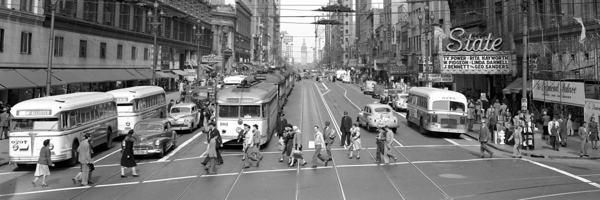 black and white photo of people crossing market street with buses and streetcars in background