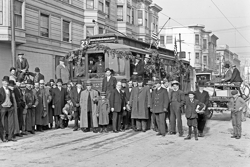 A crowd of men pose with a streetcar covered in garlands in December of 1910.
