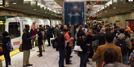 color photo showing Muni underground station platform filled with people.  To the left there is a Muni train waiting to board passengers and to the right is an empty trackway.