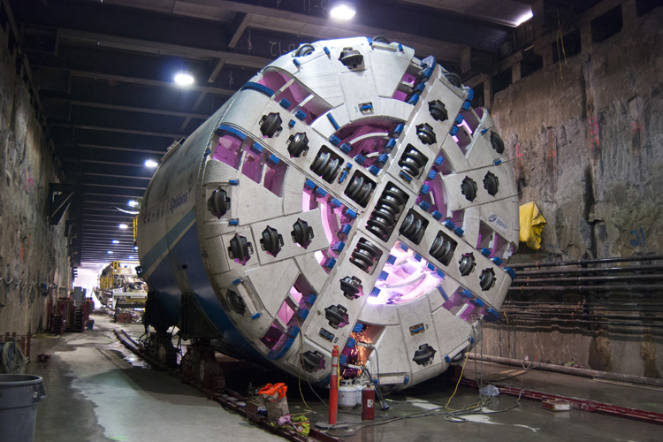 Welders work behind the face of tunnel boring machine Mom Chung, creating a pink glow. The face of the machine is called a cutter head.
