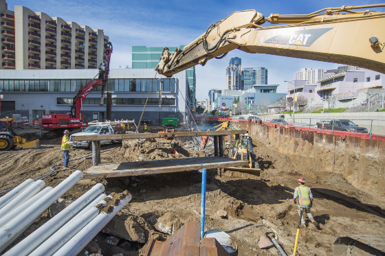 Workers lift and relocate a large trench shield as work continues on the excavation of the site at 4th and<br />
        Folsom streets.