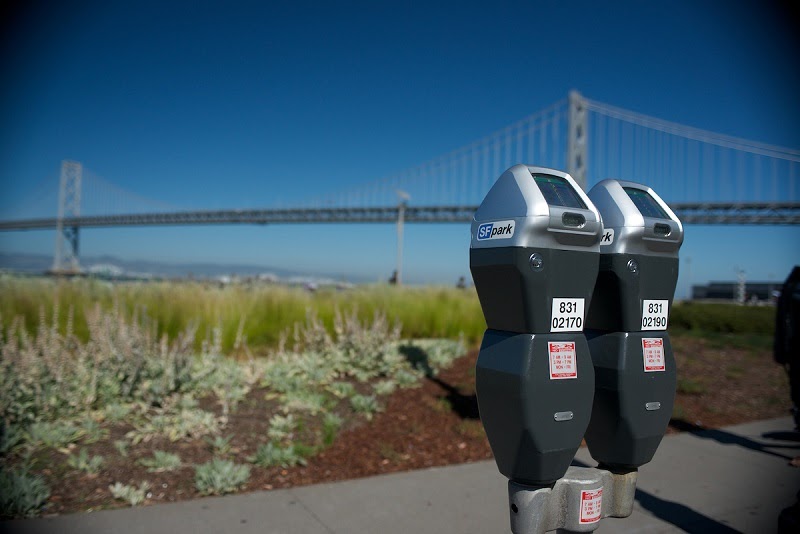 Two parking meters next to a grassy rise with the Bay Bridge in the background