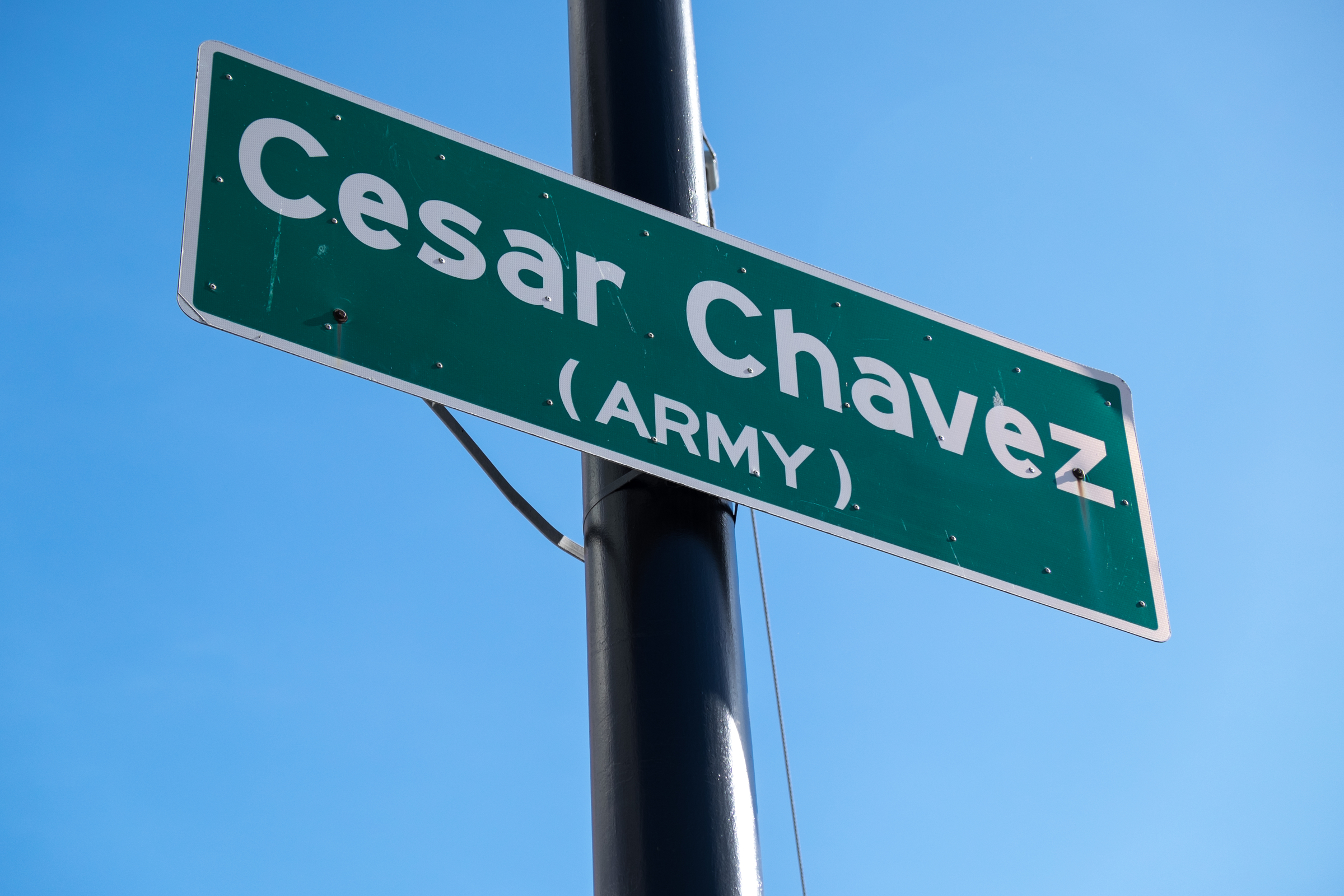 Low-angle photograph of a street sign: "Cesar Chavez (Army)" with a bright blue sky in the background