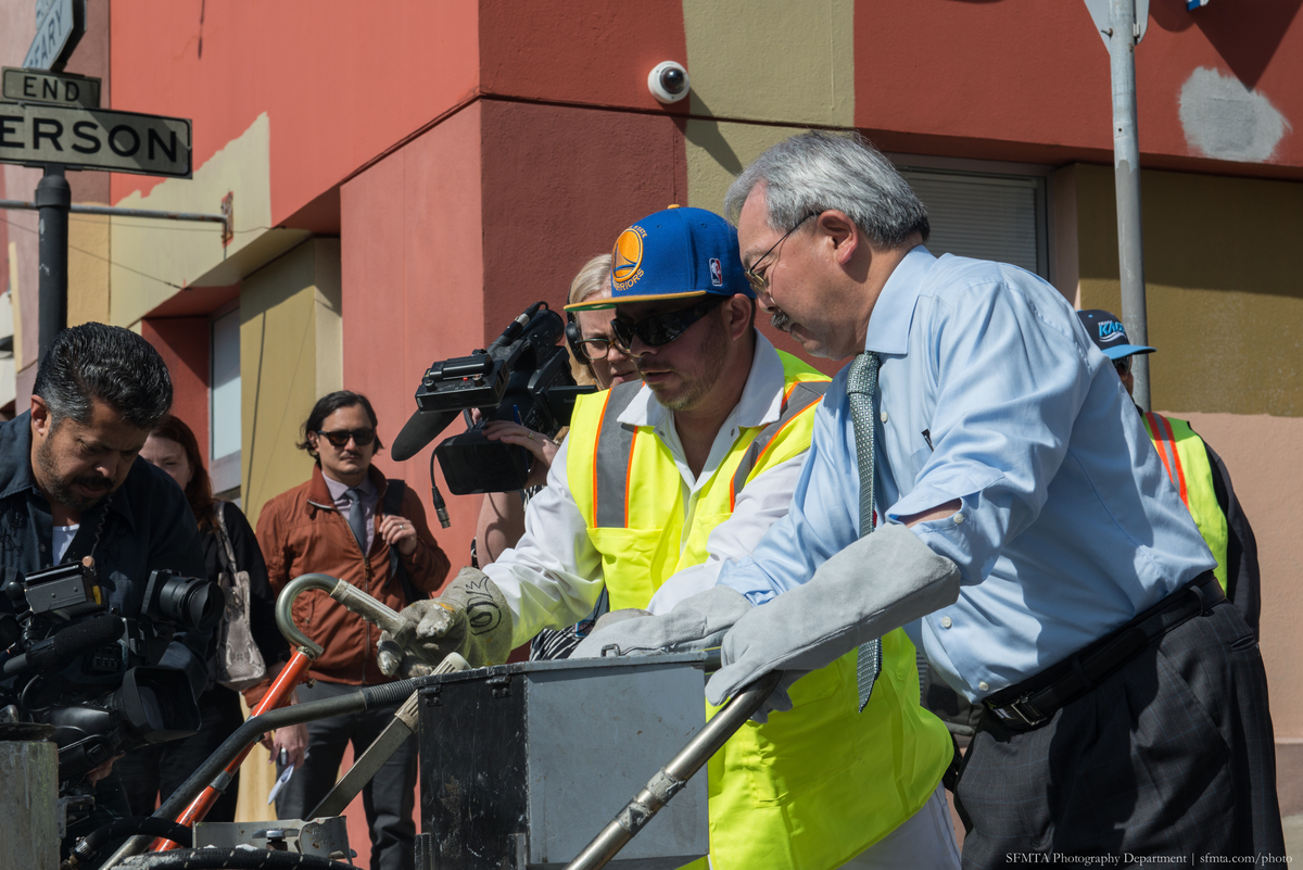 Mayor Lee and SFMTA paint shop crew member apply first pass of paint on crosswalk at Emerson and Geary while staff and media look on.