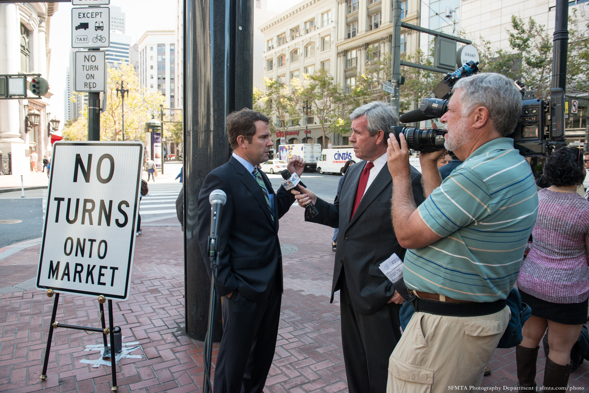 MTA Board member Malcom Heineke is interviewed by a crew from NBC at Market and O'Farrell with "No turns onto Market Street" sign in the background.