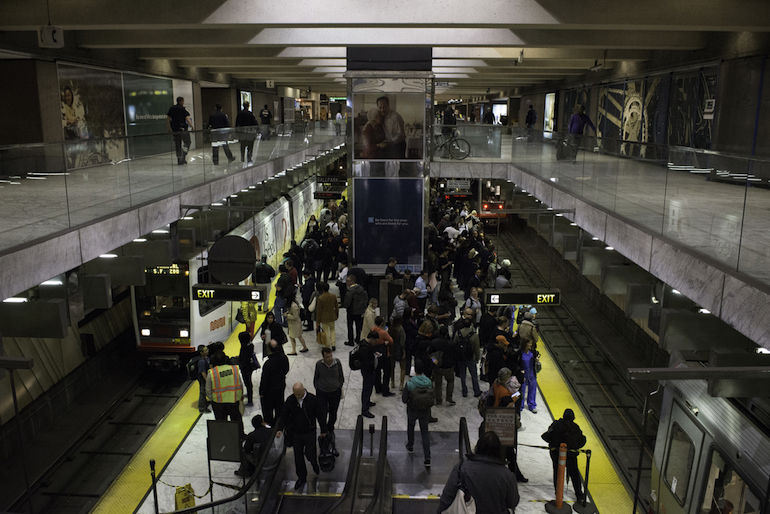 Photo shot down the escalator to show a crowd of customers waiting on the platform at Embarcadero Station.